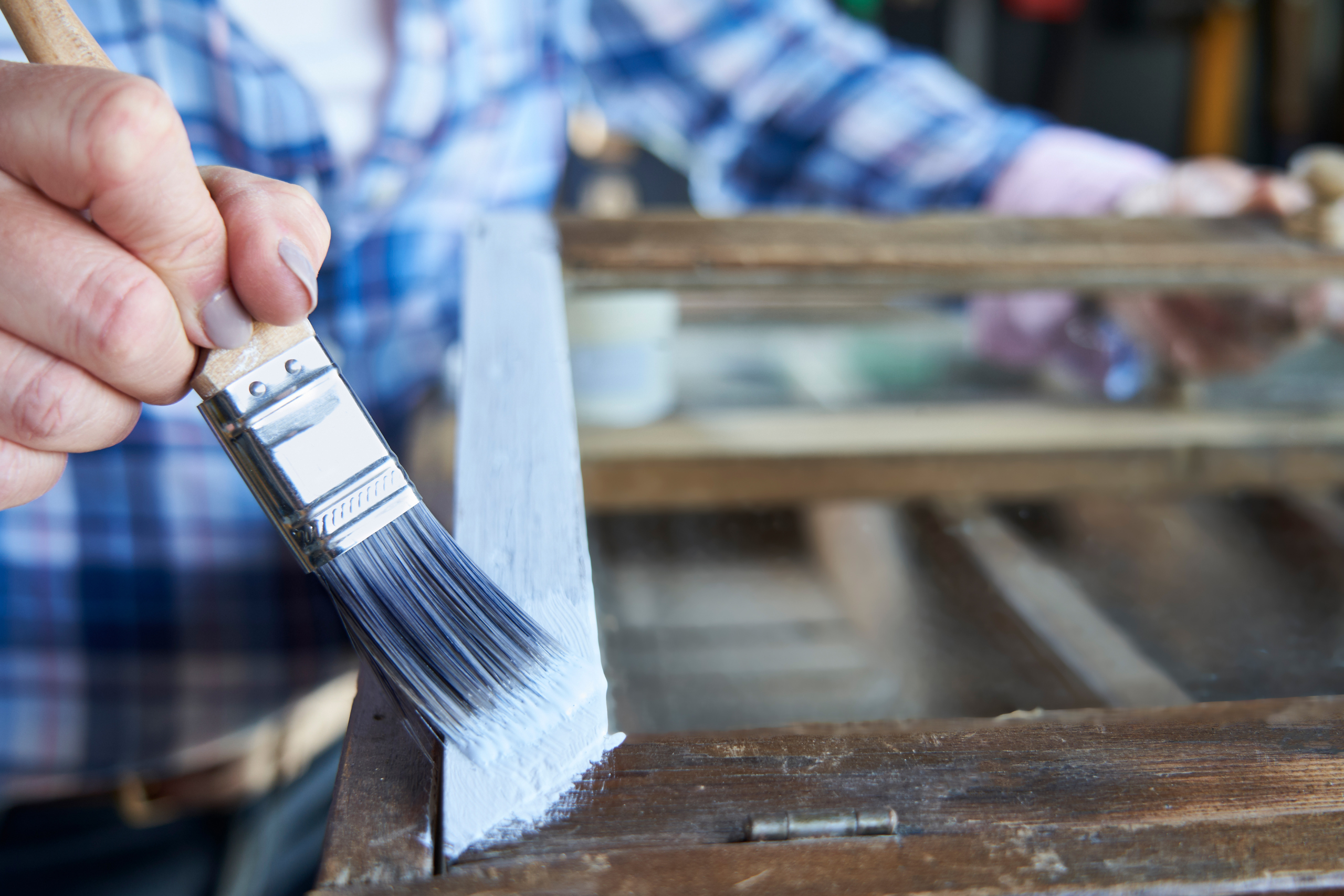 Woman painting an old window frame with blue paint at home